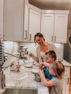 a woman and two children are in the kitchen preparing food on the counter top,