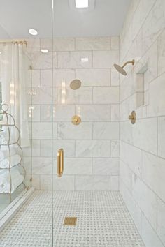 a walk in shower sitting next to a white tiled wall with gold fixtures on it