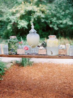 a wooden table topped with vases filled with flowers next to grass and trees in the background