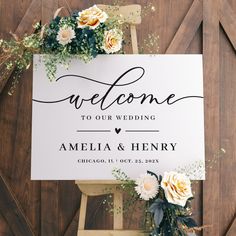 a welcome sign with flowers and greenery sits on top of a wooden easel