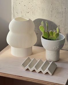 a white vase sitting on top of a wooden table next to a potted plant