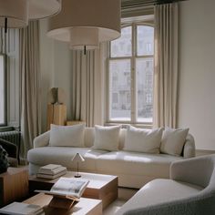 a living room filled with furniture next to a large window covered in curtains and drapes