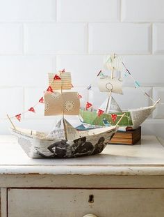 two paper boats sitting on top of a wooden dresser next to a white brick wall