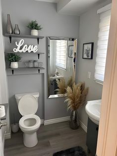 a white toilet sitting in a bathroom next to a sink under a mirror with the word love on it