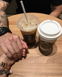 two people holding hands over a table with drinks on it and one person's arm wrapped around the other