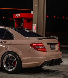 a beige car parked in front of a gas station at night with its lights on