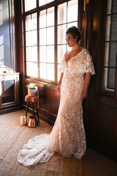 a woman standing in front of a window wearing a wedding dress and posing for the camera