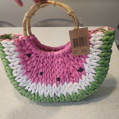 a pink, green and white woven purse with a price tag on the handle that is held by a person's hand