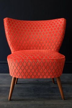 an orange chair sitting on top of a wooden floor next to a black wall in a room