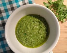 a white bowl filled with green pesto on top of a wooden table next to parsley