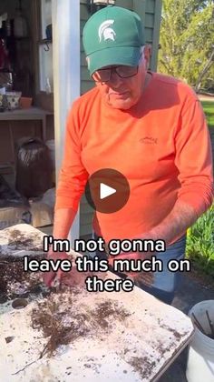 an old man is digging dirt in the yard with his hands and wearing a green hat