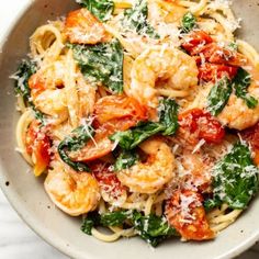 pasta with shrimp, spinach and parmesan cheese in a white bowl on a marble surface