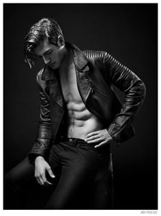 a shirtless man in black leather jacket leaning on his knees with his hands on his hips