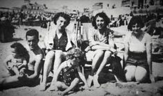 an old black and white photo of four women sitting on a bench at the beach