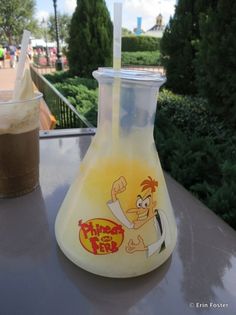 a glass beaker sitting on top of a table next to a cup filled with liquid