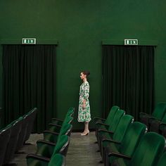 a woman in a green dress standing next to a row of green chairs with black seats