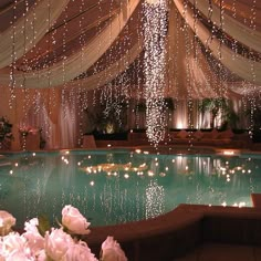 an indoor swimming pool decorated with white flowers and string lights hanging from the ceiling over it