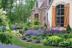 a house with lots of flowers in front of it and trees on the other side