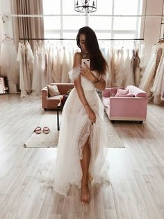 a woman in a white dress is looking at her cell phone while standing in front of a rack of dresses