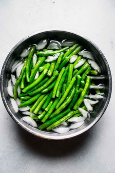 green beans and ice in a bowl on a white counter top, with water running down the side