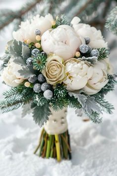 a bridal bouquet with white flowers and greenery in the snow on a snowy day