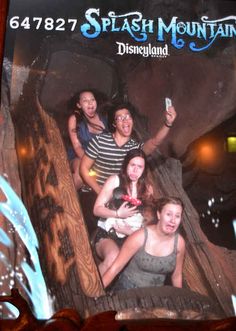 four girls are riding on a roller coaster at the amusement park while one girl is holding up her cell phone