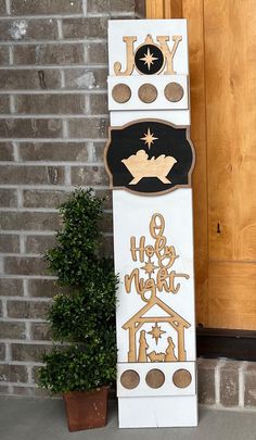 a tall white and black christmas sign sitting on the side of a building next to a potted plant