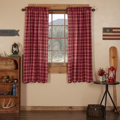 a living room filled with furniture and a window covered in red plaid curtain panels next to a wooden shelf