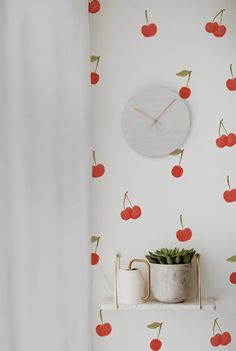 a wall clock with cherries on it next to a potted plant and vase