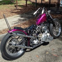 a purple motorcycle is parked on the side of the road next to a tree and fence