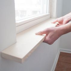 two hands are reaching for the edge of a window sill to open it up