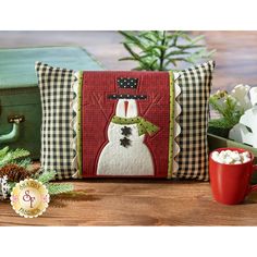 a snowman pillow sitting on top of a wooden table next to a red mug