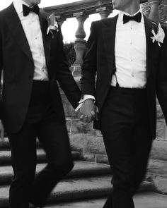 two men in tuxedos are walking down the stairs holding each other's hands