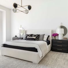 a bedroom with white walls, black and white bedding, two nightstands and a large mirror on the wall