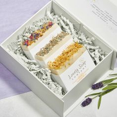 three soaps in a box with lavender flowers on the side and an envelope inside