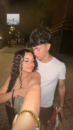 a man and woman taking a selfie on the street at night with their arms around each other