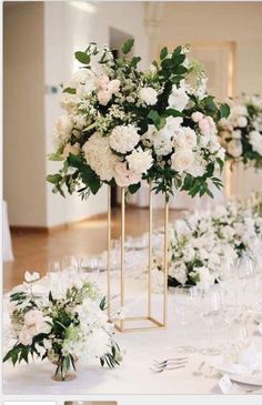 the tables are set with white flowers and greenery in gold vases on them