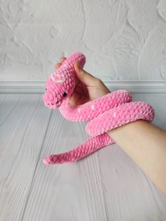 a hand holding a pink snake toy on top of a white wooden floor next to a wall