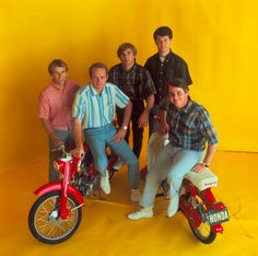 a group of men standing next to each other in front of a yellow wall with a red fire hydrant