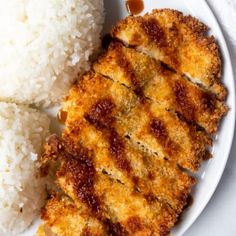 two pieces of fried chicken on a white plate with rice and sauce next to it