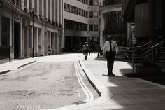 black and white photograph of people walking down the street in an urban area with tall buildings