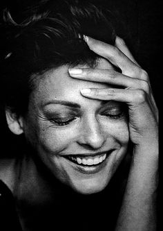 a black and white photo of a smiling woman with her hands on her head,