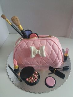 a cake that is shaped like a purse and has makeup on the table next to it