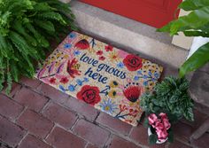 a door mat that says, love grows here next to some plants on the sidewalk