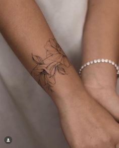 two hands holding each other with tattoos on their wrists and wrist, one has a flower tattoo on it