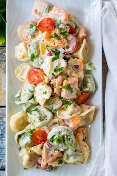 a white plate topped with pasta and shrimp salad next to a napkin on top of a wooden table