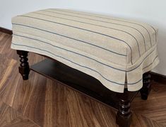 a wooden bench with a striped cover on it's seat and wood flooring