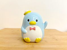 a blue and white penguin with a bow tie on it's head sitting on a wooden table