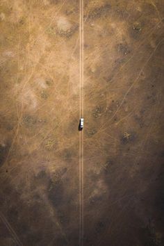 an aerial view of a car driving down a dirt road in the middle of nowhere