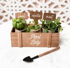 a wooden box filled with plants on top of a white table next to a shovel